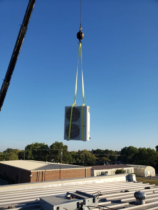 Crane lifting a large HVAC unit onto a commercial rooftop under a clear sky