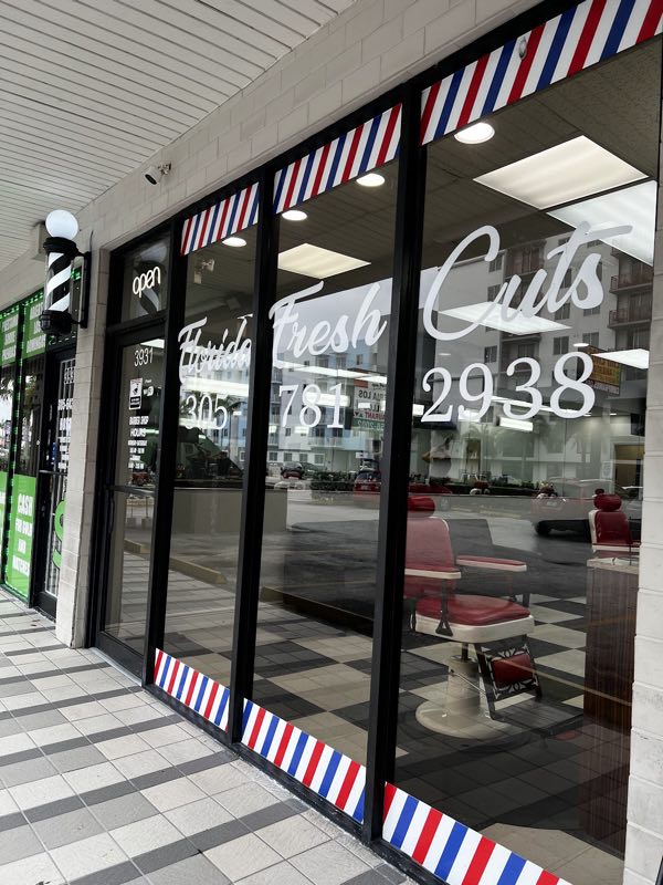 Florida Fresh Cuts storefront: shop name lettered on the window, barber pole and open sign, red chair visible inside