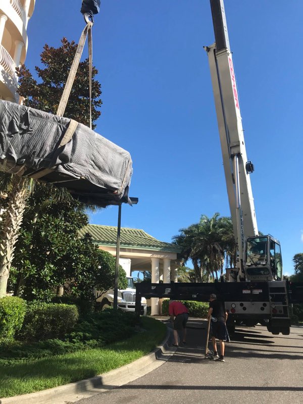 Crane hoisting a wrapped piece at a condo under a blue Florida sky