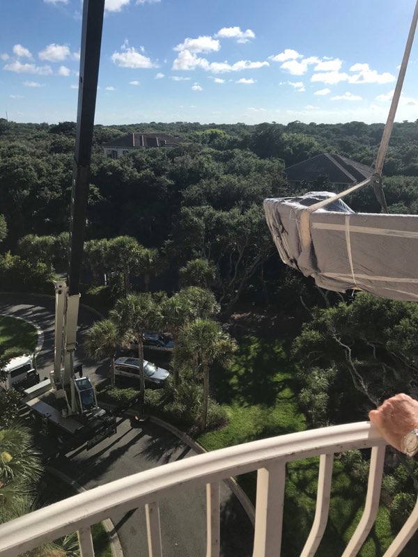 Balcony crane hoist mid-lift, a wrapped item rising above the palms