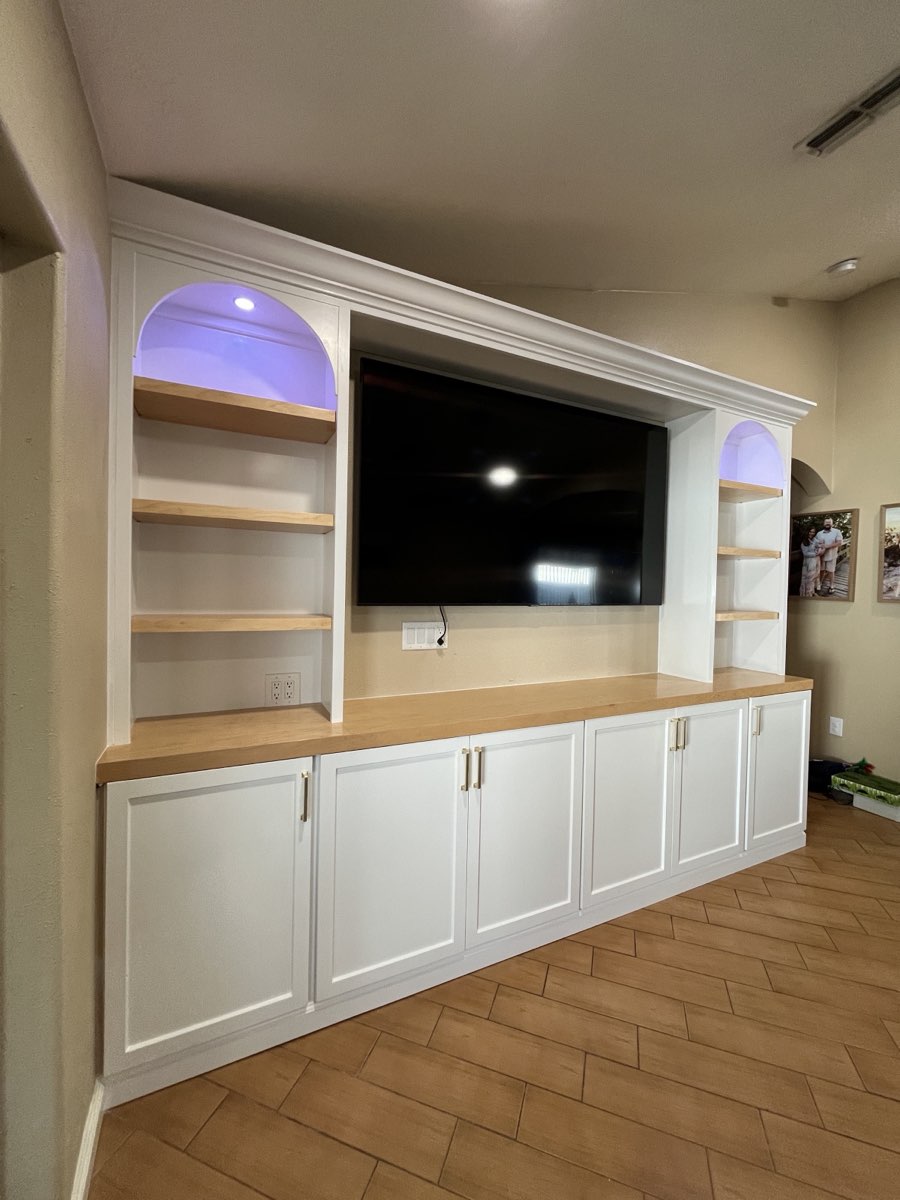Custom white entertainment center with arched, LED-lit display niches and a natural wood surface, built by Frost Custom Carpentry
