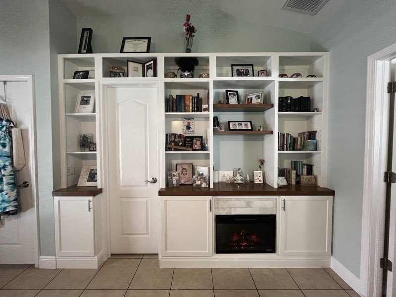 White built-in bookshelves and cabinetry surrounding a doorway with a stone-fronted electric fireplace