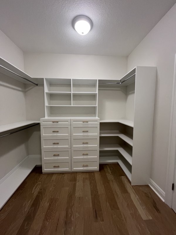 Custom white walk-in closet with a central bank of drawers, corner shelving and hanging rails