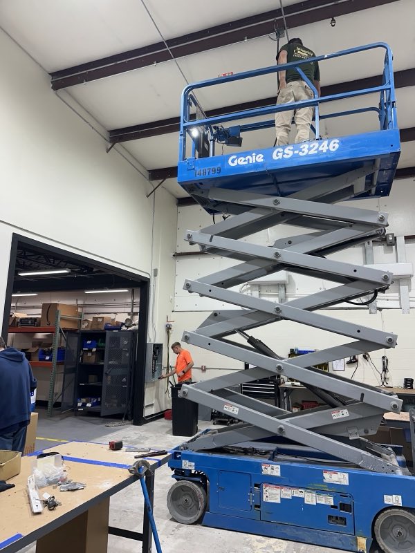 Electrician working from a scissor lift on high-bay wiring inside a warehouse