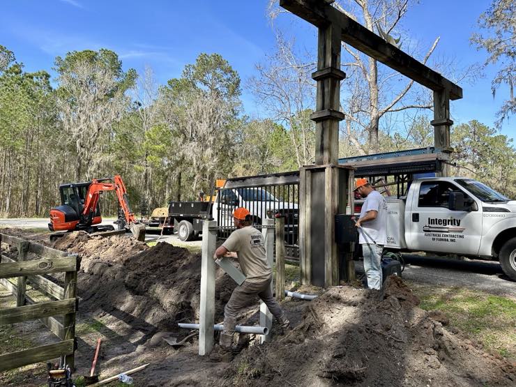 Integrity Electrical crew setting a pole at an entrance gate with trucks on site