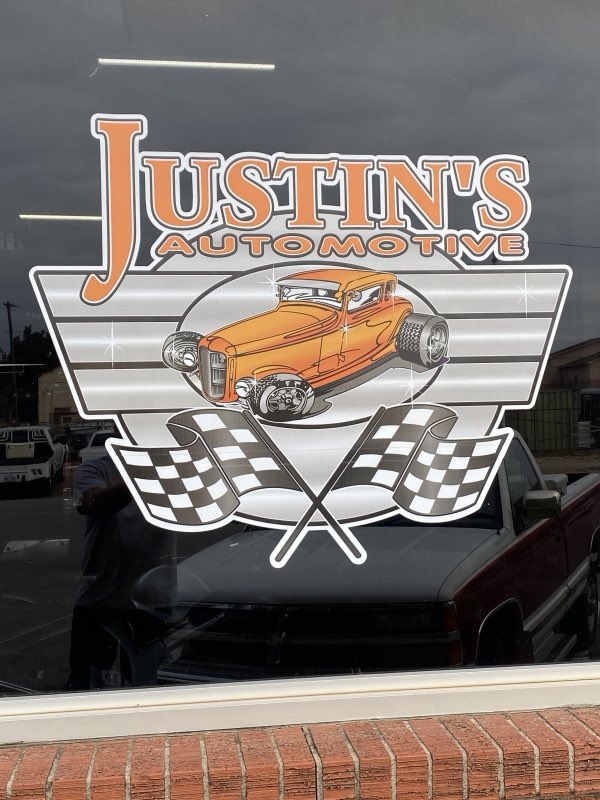 Justin's Automotive hot-rod logo with checkered flags lettered on the front window