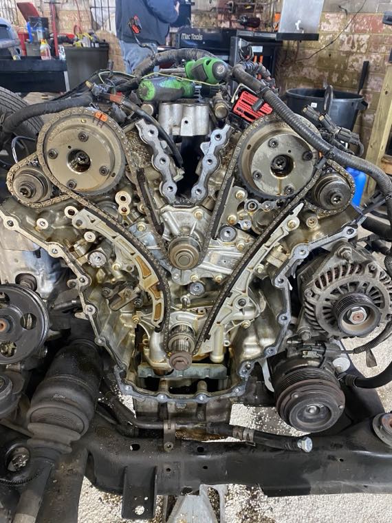 Close-up of a V6 engine with the timing cover removed, showing the timing chains and gears