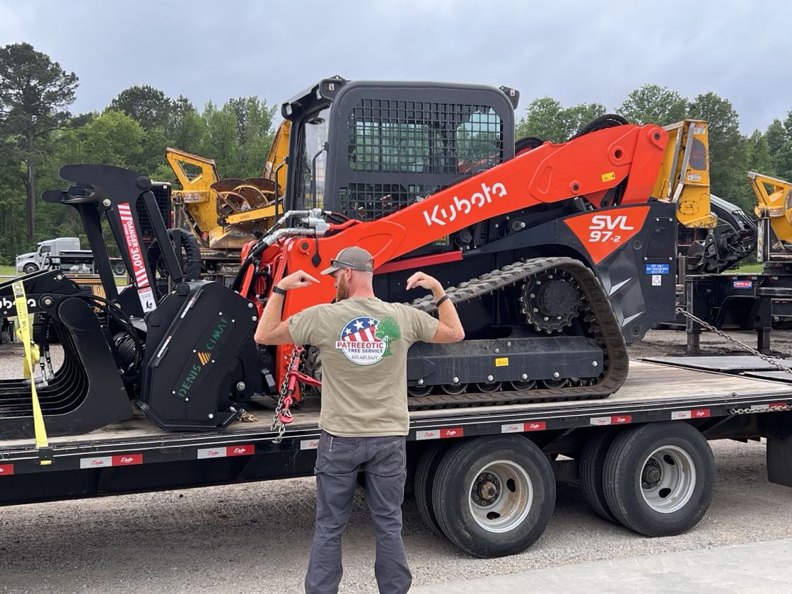 Patreeotic Tree Service crew member in a branded shirt beside the Kubota SVL97 skid-steer and forestry mulcher loaded on the trailer