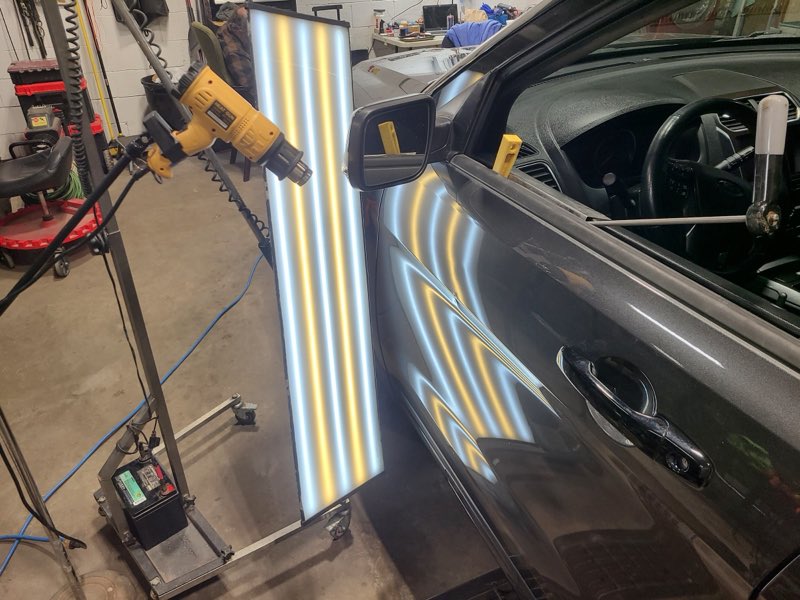 Light reflection board held against a car door to reveal dents during paintless dent repair