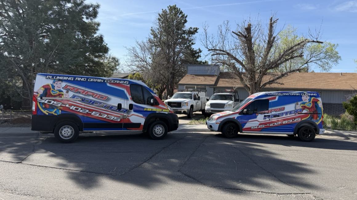 Two wrapped Rapid Rooter vans parked front to front in Farmington, both reading Plumbing and Drain Cleaning, 505-402-6335, 24 Hour Emergency Service.