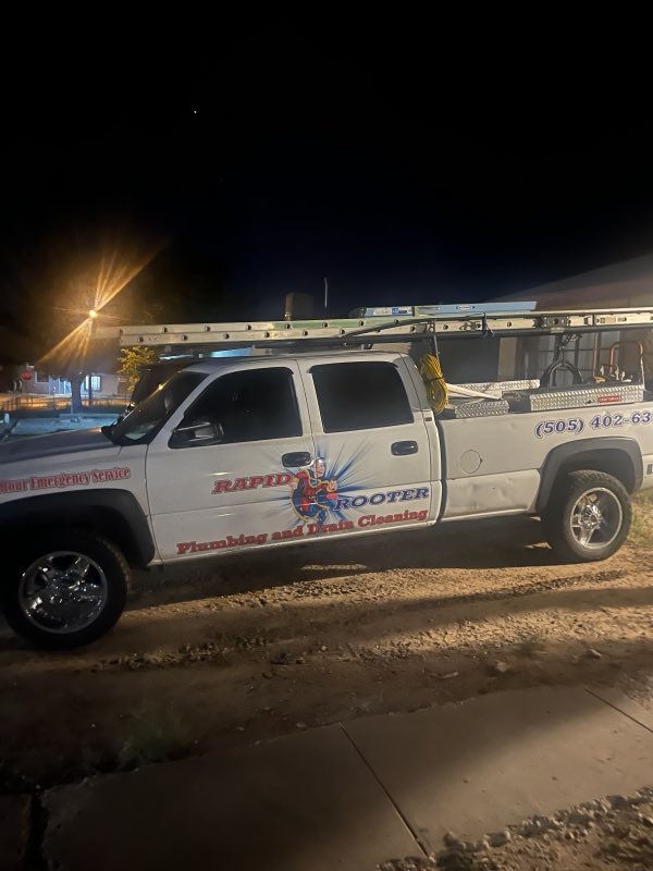 A Rapid Rooter work truck with a ladder rack and reels of cable parked at night on an after-hours emergency call.