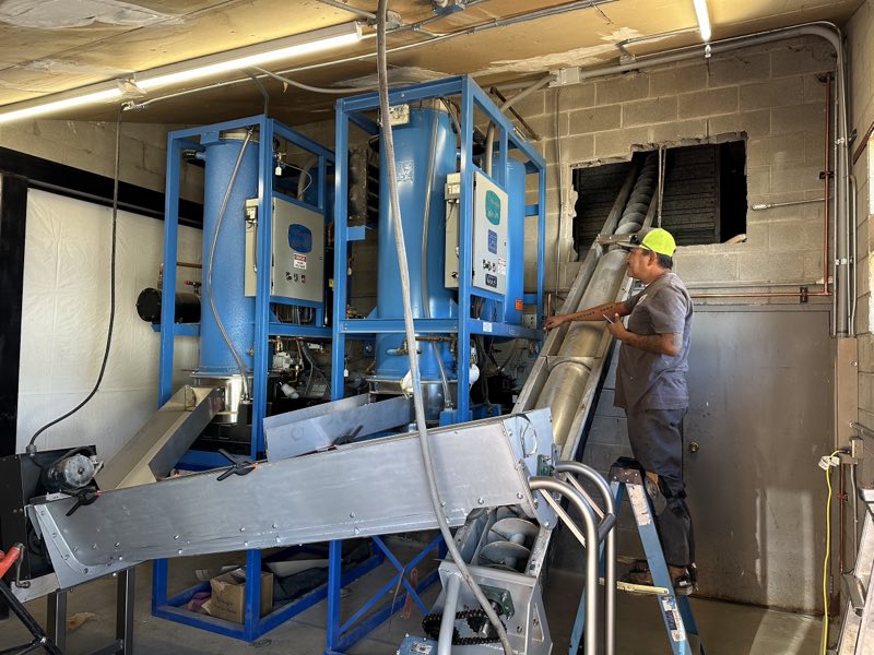 A Rapid Rooter technician on a ladder servicing large blue commercial mechanical equipment.