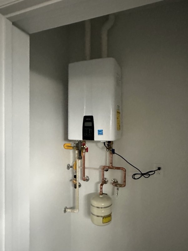 A wall-mounted tankless water heater installed with neat copper piping and an expansion tank.