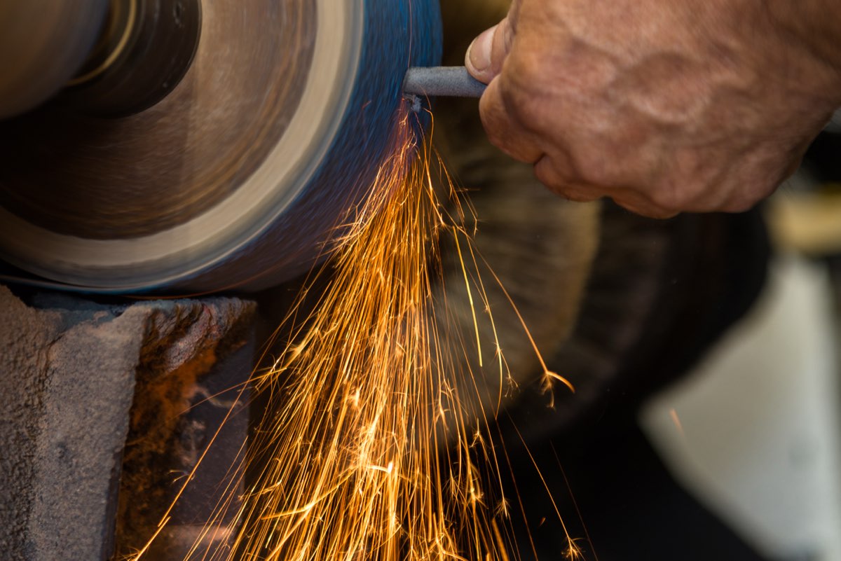 Craftsman finishing a sole at the wheel, sparks flying, at Shoe Repair and Beyond
