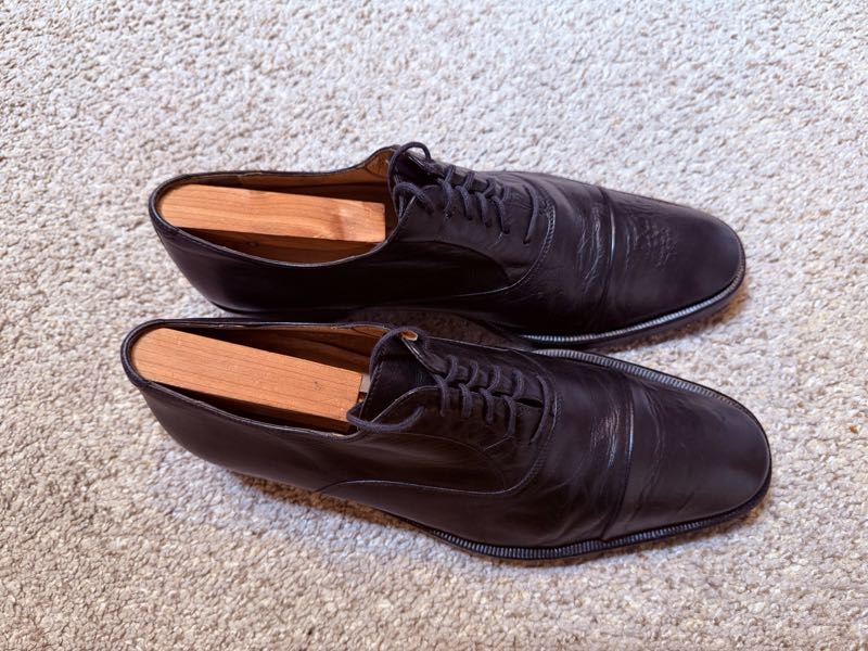 A pair of restored dark leather dress shoes with wooden shoe trees.