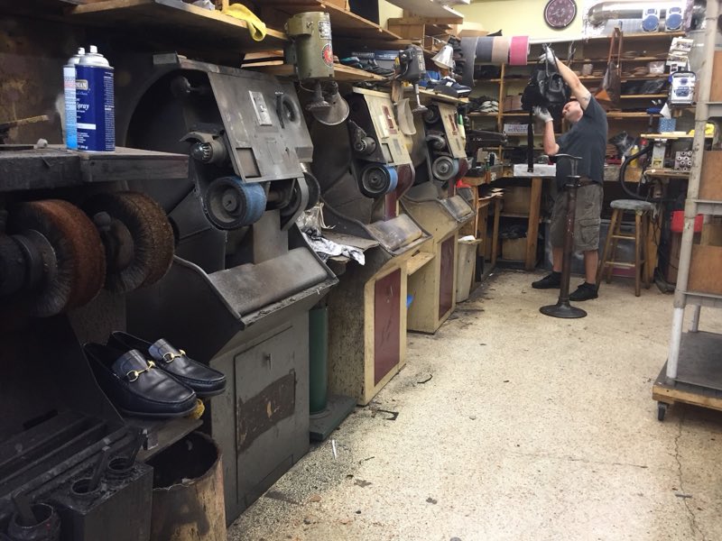 Row of shoe-repair finishing machines with a craftsman working at the back of the shop.