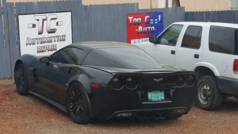Black Corvette parked in front of the TC Automotive Repair and Too Cool Auto banners