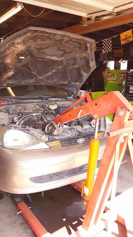 Engine swap in progress inside the garage, car raised on a hoist with the hood open